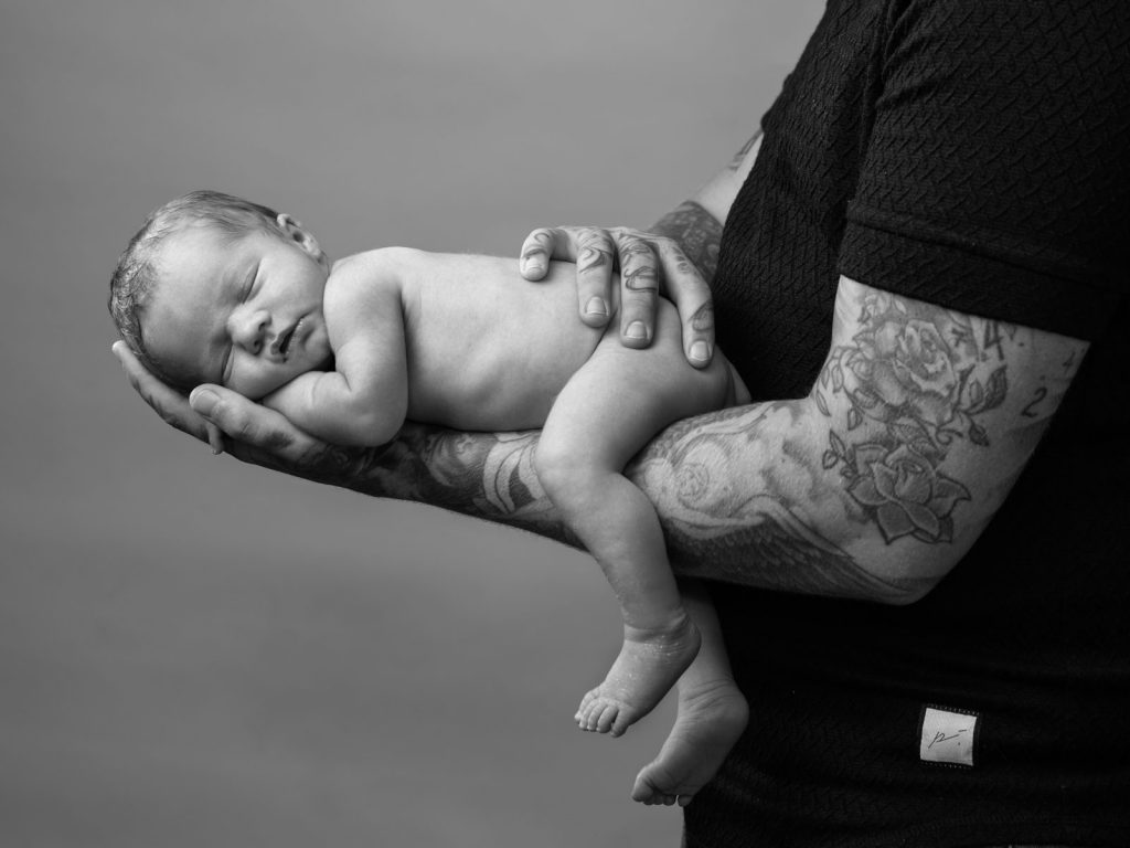 newborn baby with dad's arms holding him
