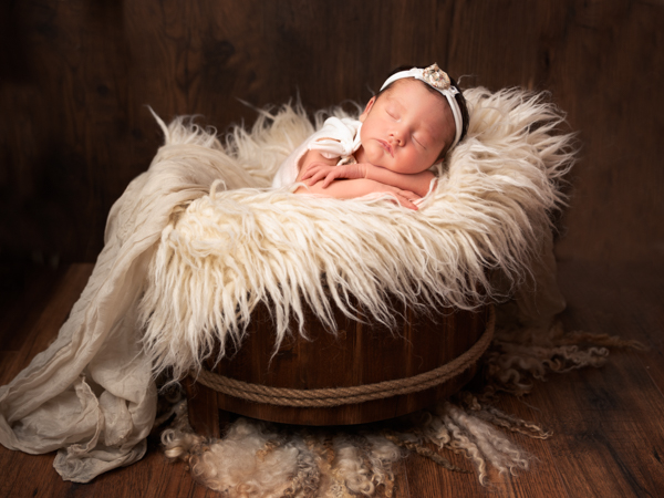 textured photoshoot of newborn baby in wooden barrel