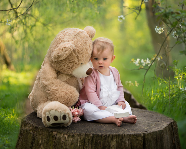 baby girl on tree stump with teddy