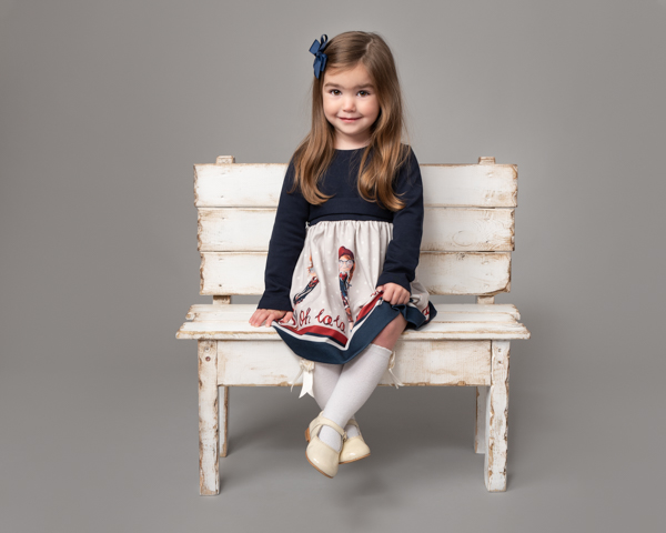 little girl with blue bow on white bench