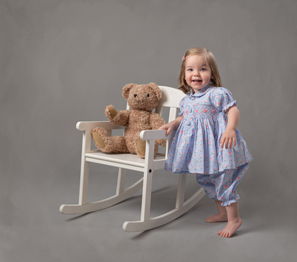 little girl with her teddy sat in a chair
