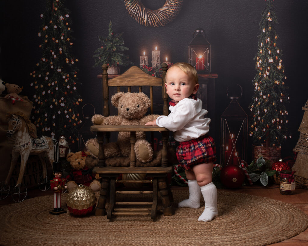Baby in Spanish Christmas outfit standing with teddy in wooden highchair