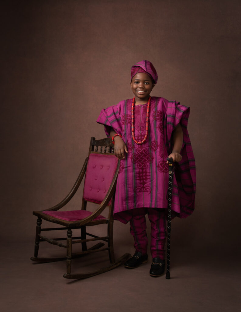 Nigerian boy in his traditional purple wear standing next to a chair