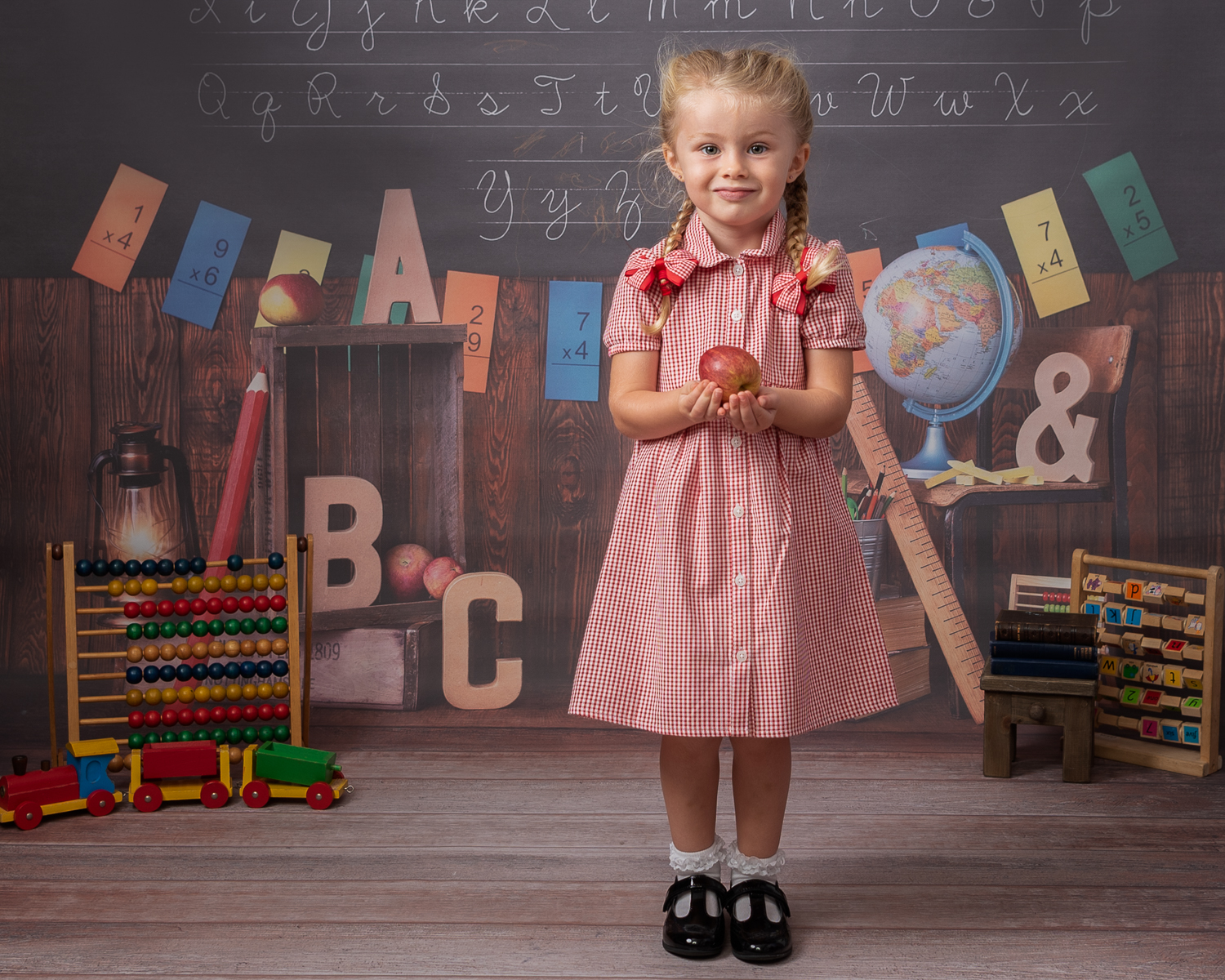 Girl in red gingham dress holding apple in back to school photoshoot